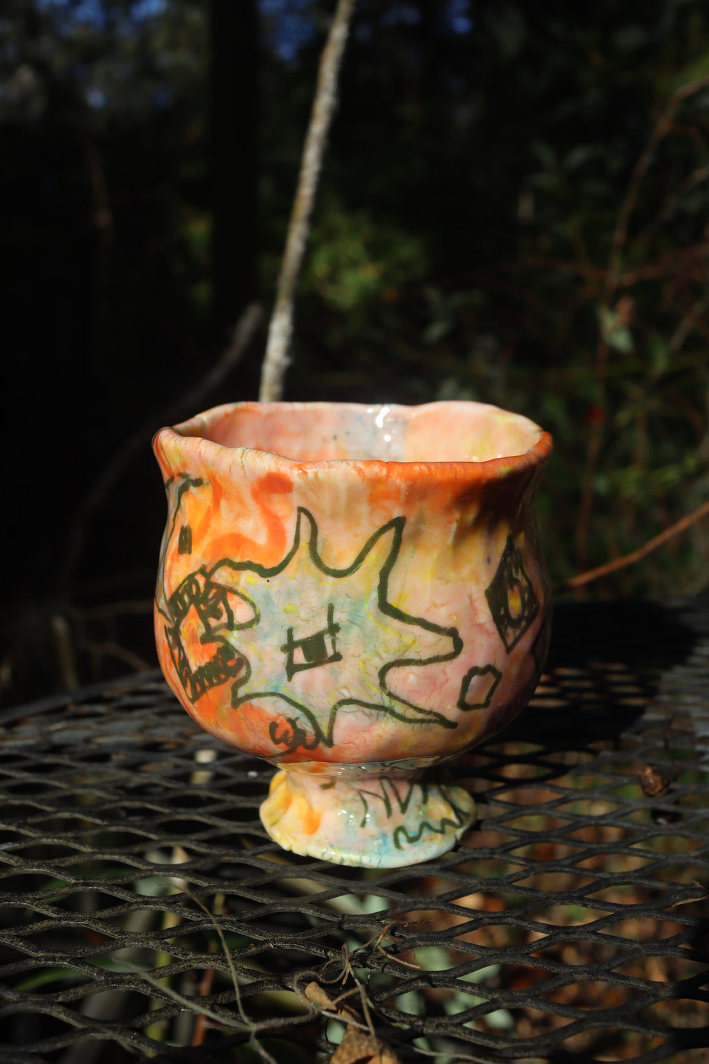 Handmade ceramic pot with artistic designs on a metal surface outdoors